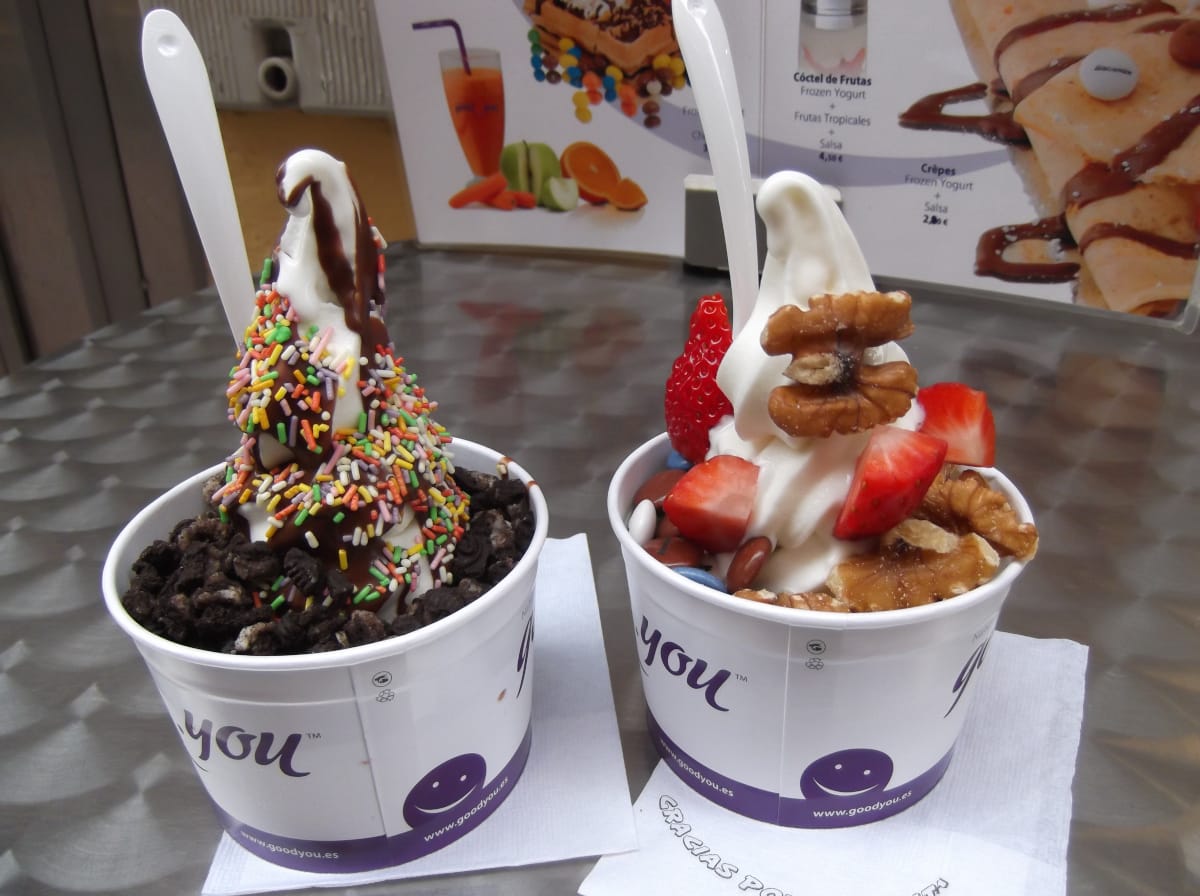zwei Eisbecher mit Softeis, eins mit Schokobrownie und bunten Streuseln, im zweiten Becher Erdbeeren und Walnüsse